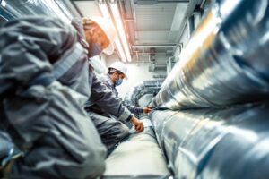 Travailleurs en uniforme vérifiant des tuyaux métalliques dans un local technique