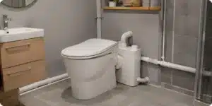 Sanibroyeur installé dans une salle de bain avec tuyauterie visible