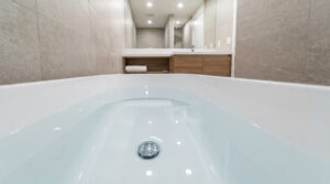Vue plongeante dans une baignoire blanche remplie d'eau stagnante dans une salle de bain moderne aux tons beige.