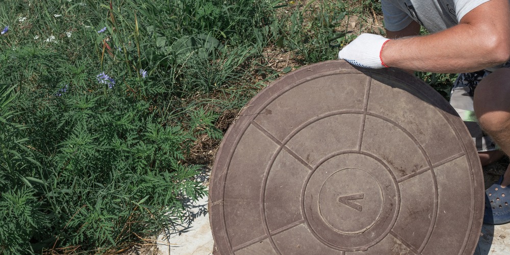 Plaque d'un regard enterré soulevée dans un jardin pour accéder au réseau d'évacuation des eaux usées