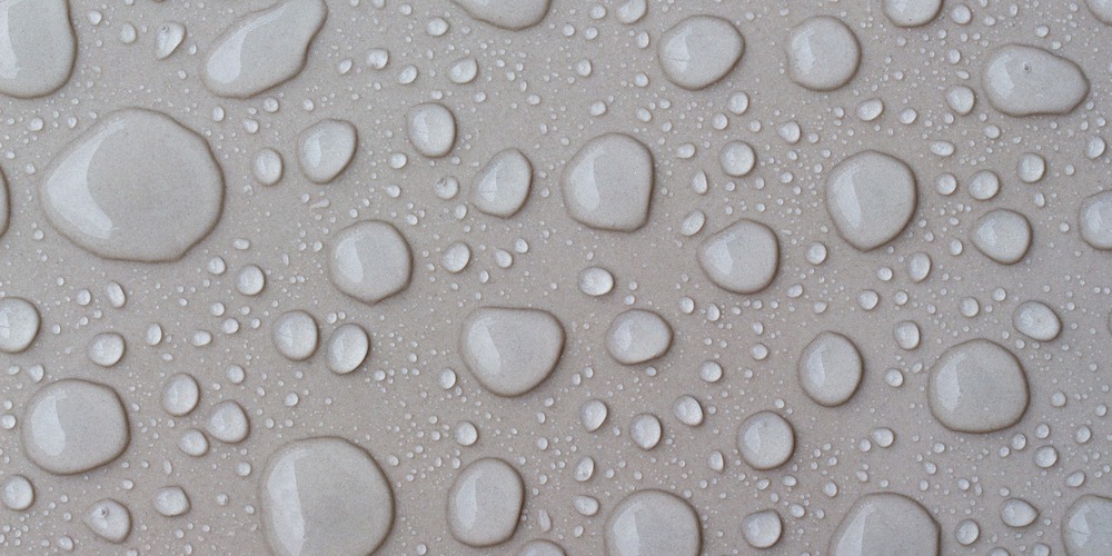 Gouttes d'eau perlant sur une surface en pierre claire, l'effet recherché quand on applique un hydrofuge